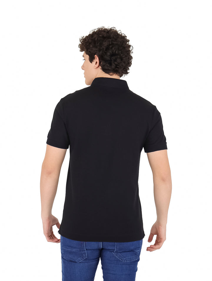 Hombre vistiendo una playera polo Lacoste de color negro y pantalones vaqueros azules.