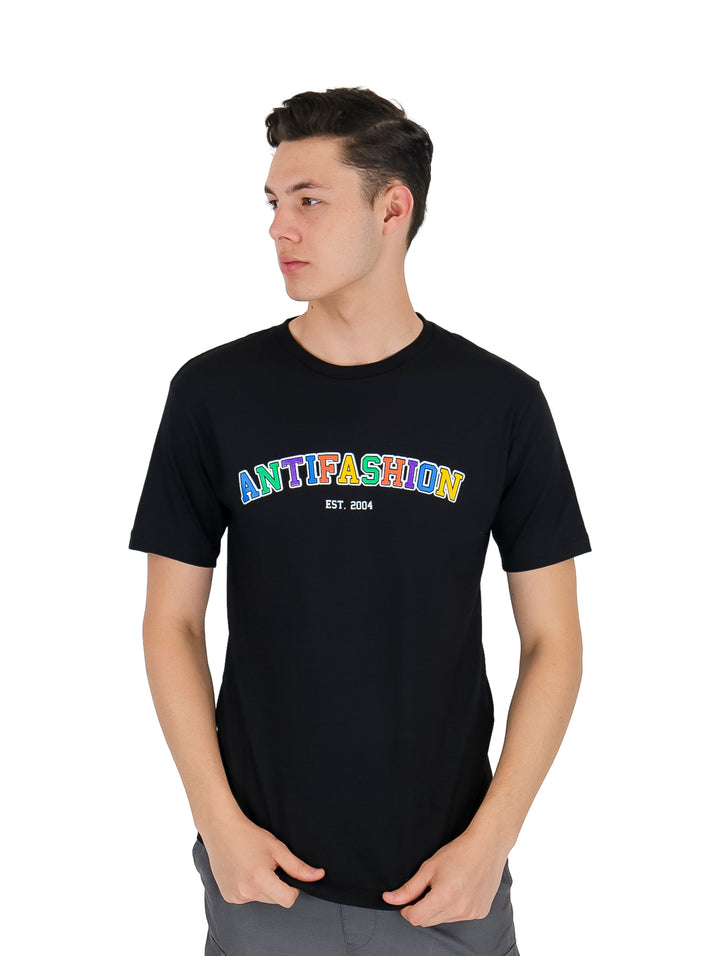 Hombre vistiendo playera negra de manga corta con el texto ANTIFASHION en colores multicolores en el pecho.
