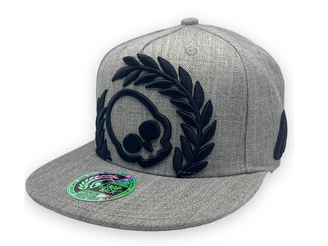 Gorra snapback color gris con diseño bordado en negro de una calavera y laureles en el frente.