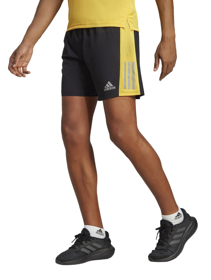 Hombre vistiendo shorts deportivos Adidas color negro con detalles laterales en amarillo y gris.