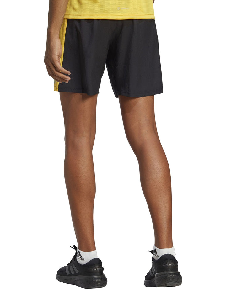 Hombre vistiendo shorts deportivos Adidas color negro con detalles laterales en amarillo y gris.
