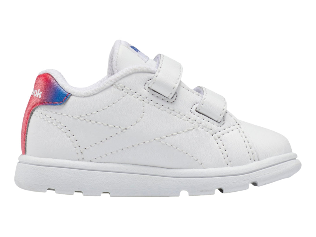Tenis deportivos blancos Reebok para niño con cierres de velcro y detalle degradado en rojo y azul en el talón.