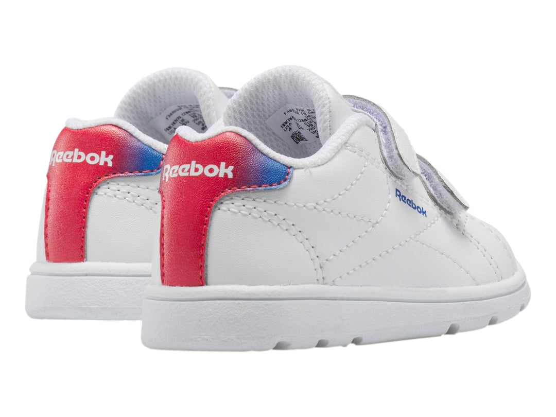 Tenis deportivos blancos Reebok para niño con cierres de velcro y detalle degradado en rojo y azul en el talón.