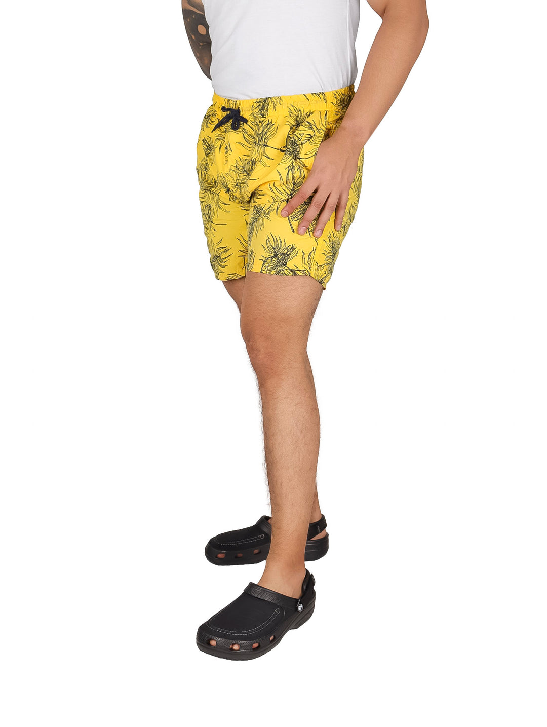 Hombre vistiendo un traje de baño corto color amarillo con estampado oscuro.