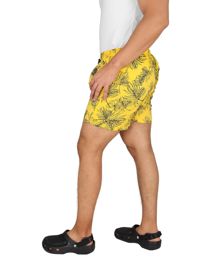 Hombre vistiendo un traje de baño corto color amarillo con estampado oscuro.