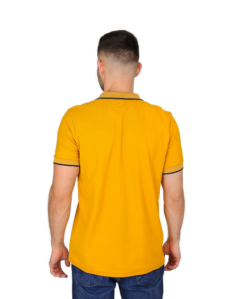 Hombre vistiendo playera polo color mostaza con detalles oscuros en el cuello y los bordes de las mangas.