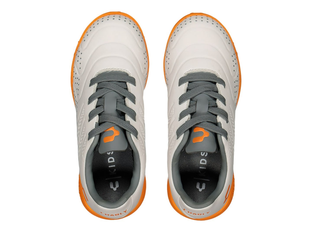 Tenis de fútbol Charly color blanco con suela naranja y detalles en gris.