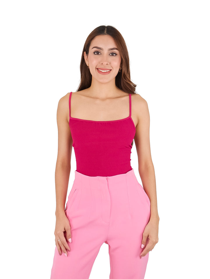 Mujer vistiendo una blusa ajustada de color rosa fucsia con tirantes delgados y pantalones rosas.