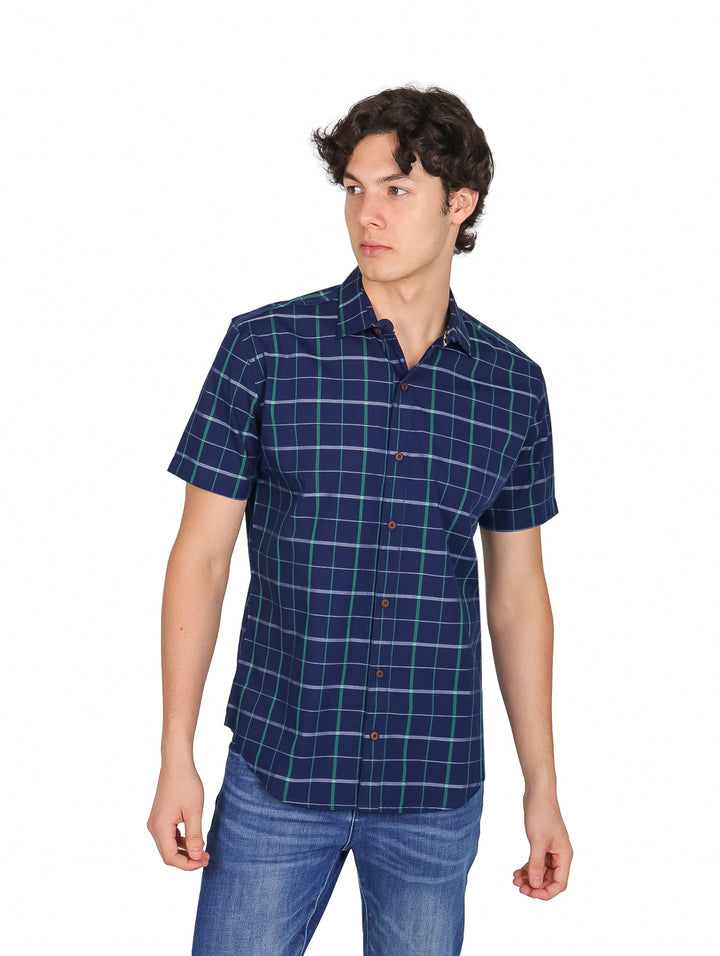 Hombre vistiendo una camisa de manga corta color azul marino con estampado de cuadros verdes y jeans azules.