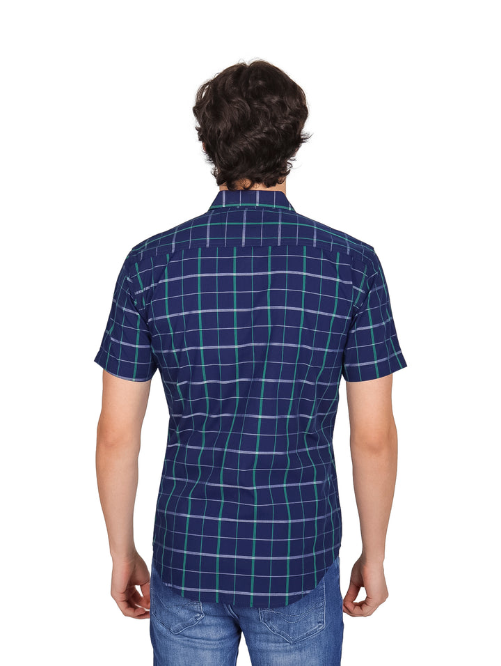 Hombre vistiendo una camisa de manga corta color azul marino con estampado de cuadros verdes y jeans azules.