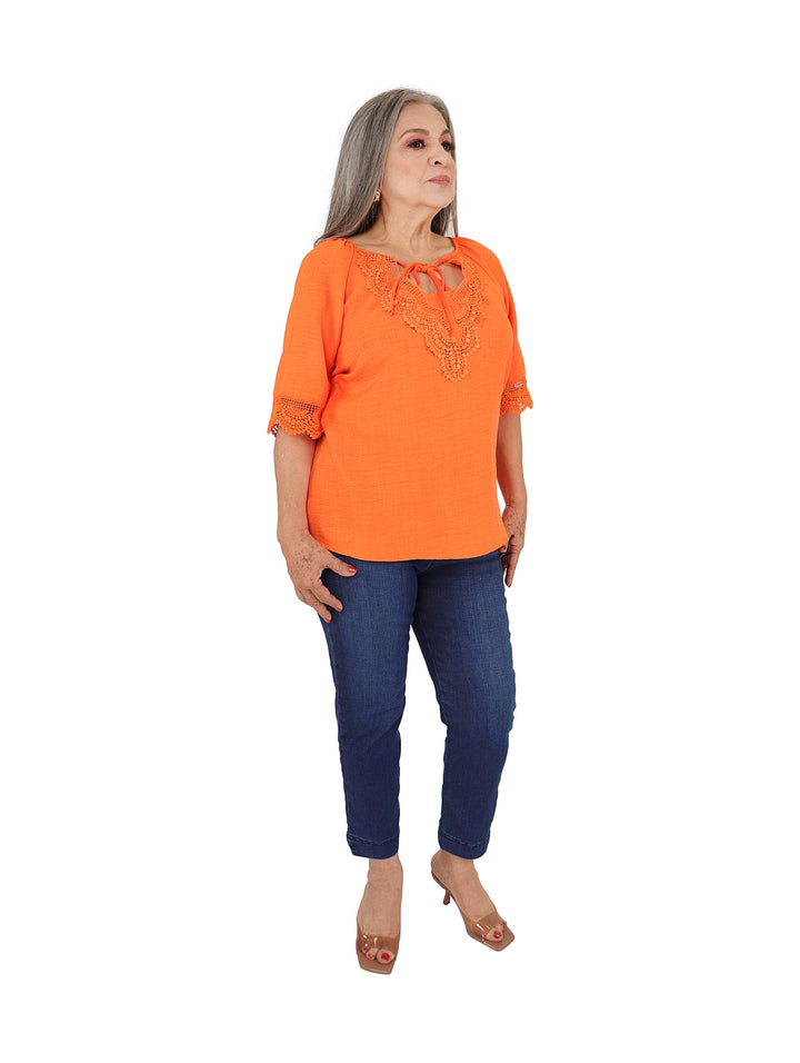 Mujer vistiendo blusa color naranja con detalles de encaje en el pecho y mangas.
