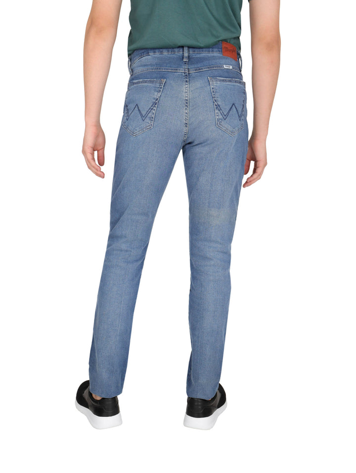 Hombre vistiendo pantalones jeans Wrangler azul claro de corte slim.