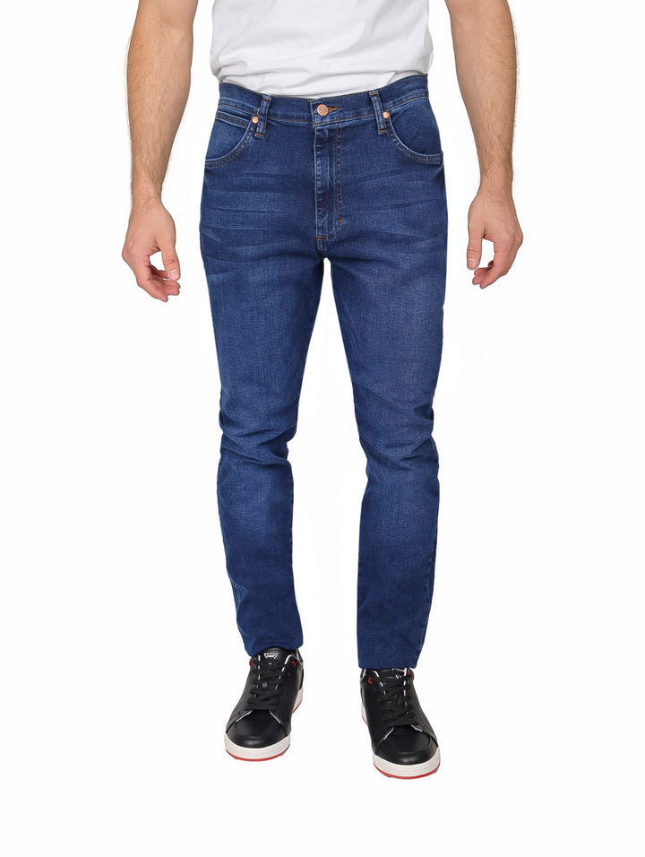 Hombre vistiendo pantalones jeans Wrangler de color azul oscuro, corte slim fit.