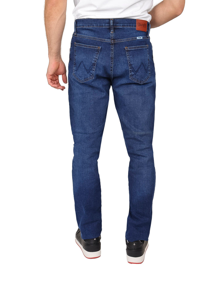 Hombre vistiendo pantalones jeans Wrangler de color azul oscuro, corte slim fit.