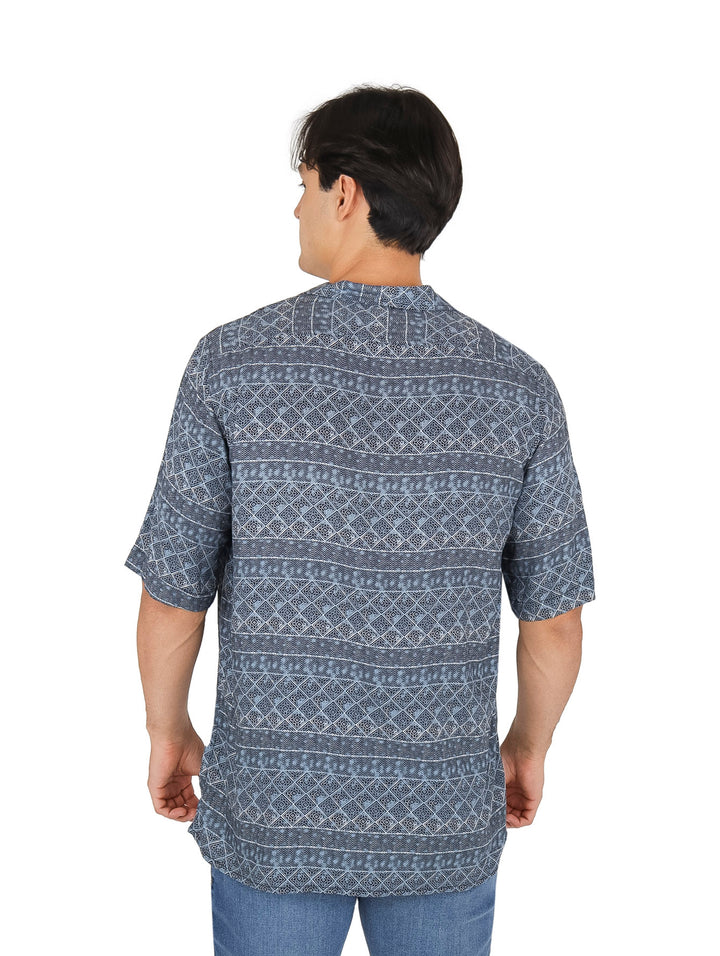 Hombre vistiendo camisa azul de manga corta con estampado étnico geométrico en color blanco y botones frontales.