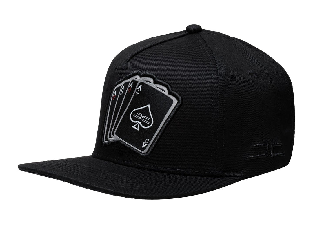 Gorra negra JC HATS con visera plana y un bordado frontal de cuatro cartas de póker.
