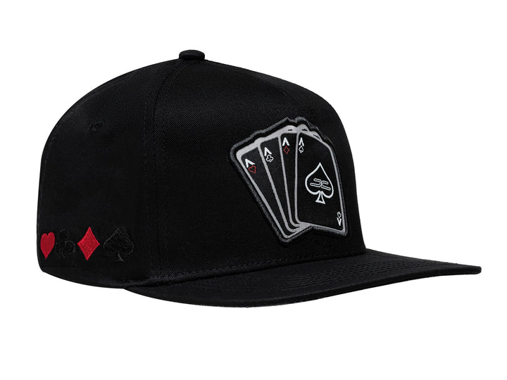 Gorra negra JC HATS con visera plana y un bordado frontal de cuatro cartas de póker.