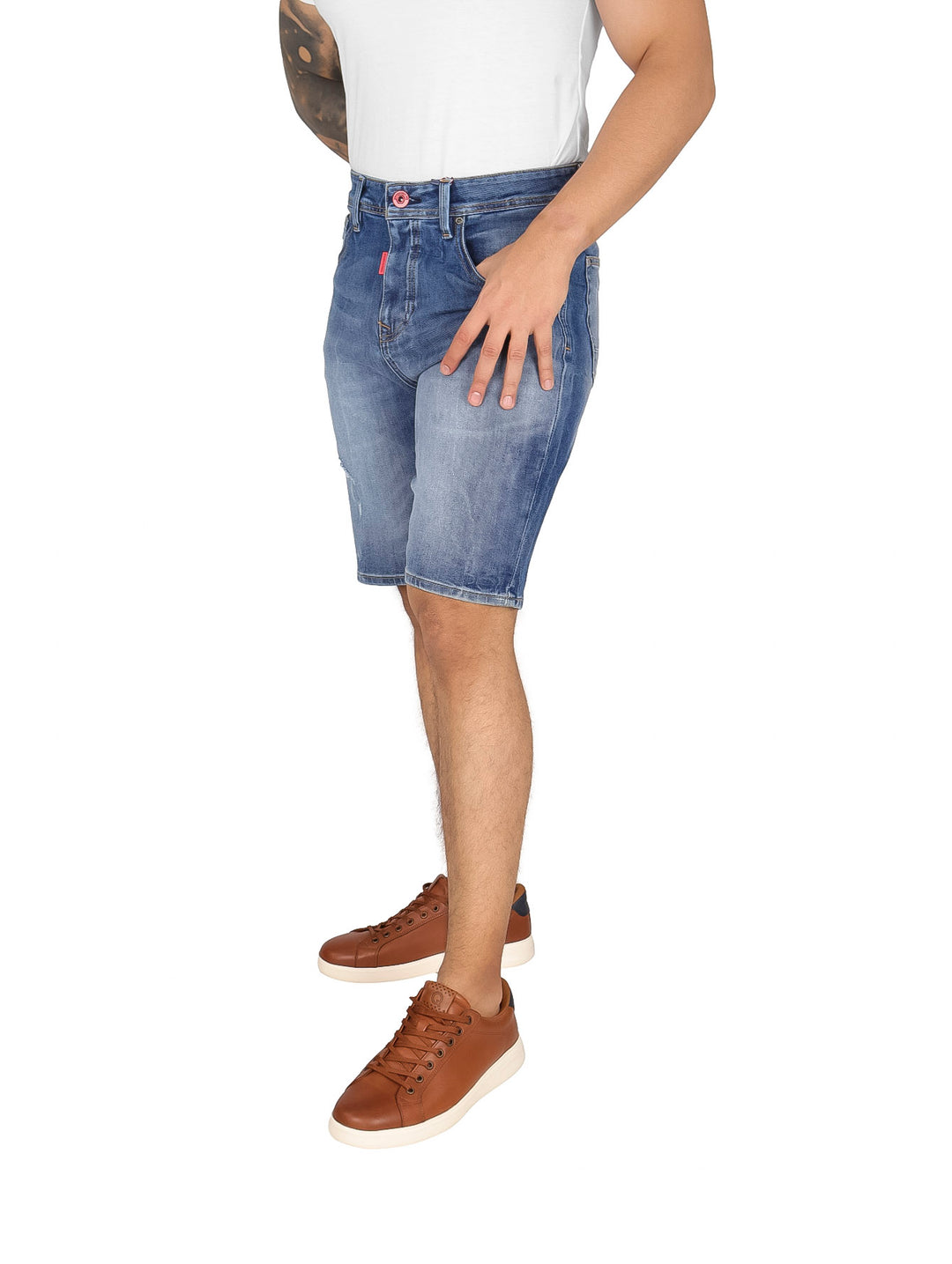 Hombre vistiendo bermudas de mezclilla azul con efecto de lavado stone y tenis color café.