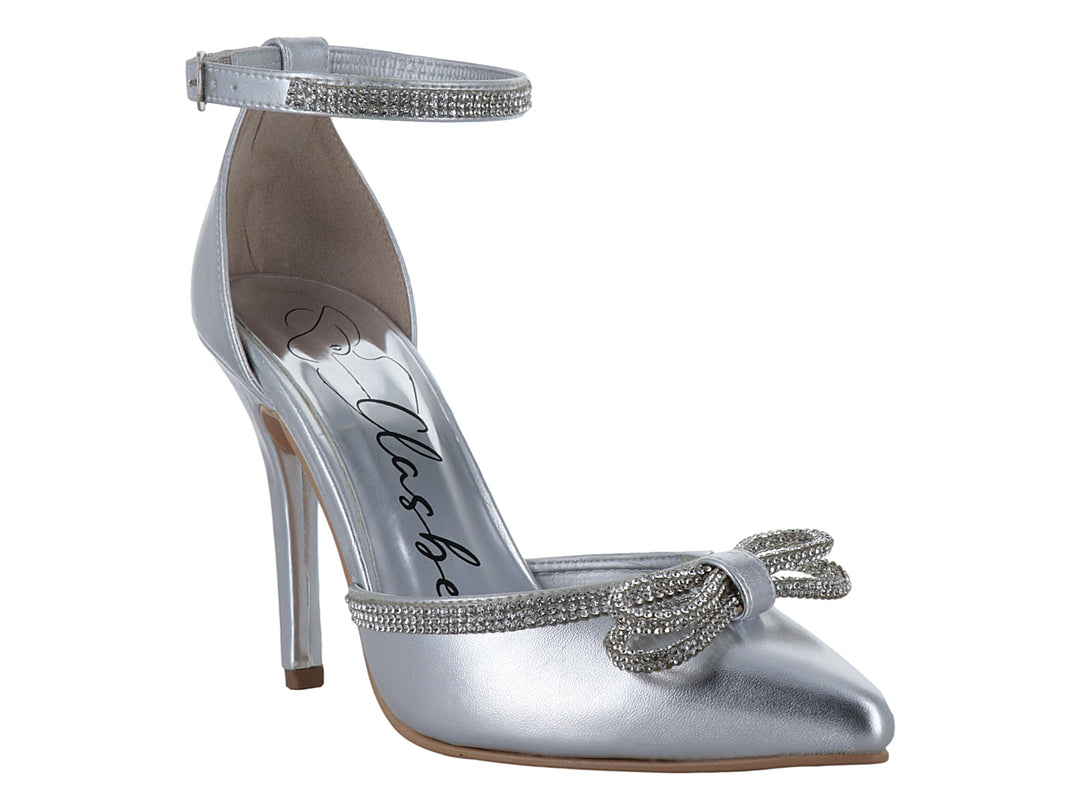 Zapato de tacón alto color plata con punta cerrada, moño decorativo y correa al tobillo con detalles brillantes.