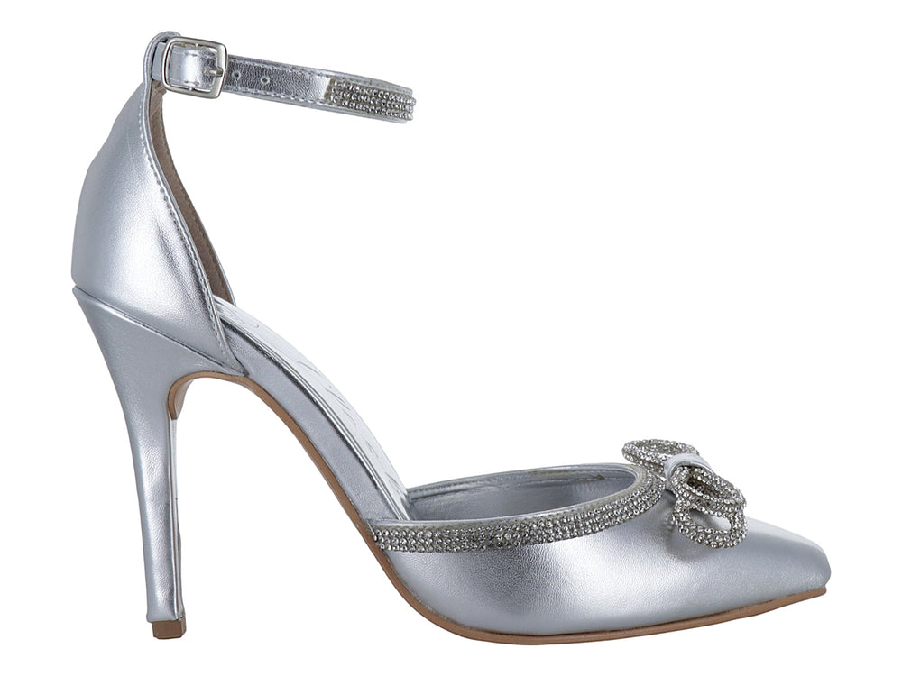 Zapato de tacón alto color plata con punta cerrada, moño decorativo y correa al tobillo con detalles brillantes.