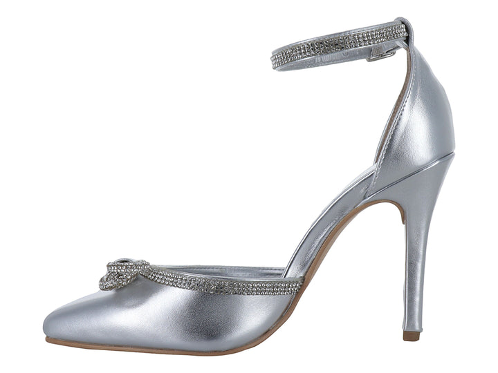 Zapato de tacón alto color plata con punta cerrada, moño decorativo y correa al tobillo con detalles brillantes.