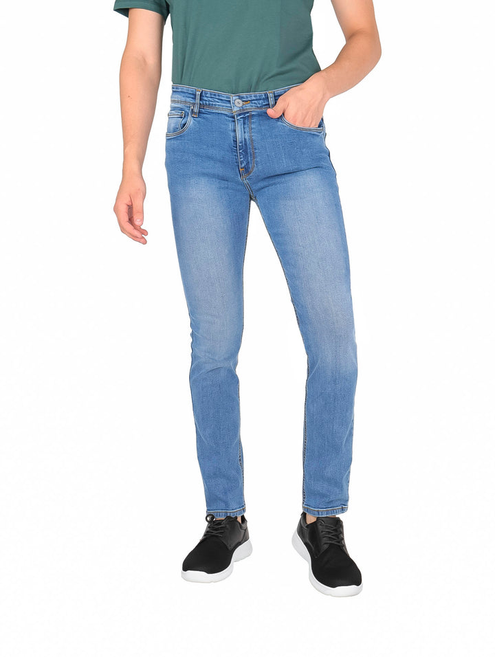 Hombre vistiendo pantalones jeans de color azul claro, camiseta verde y tenis negros.