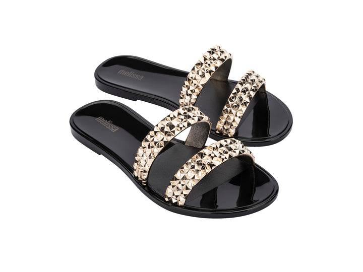 Sandalias negras Melissa con tiras adornadas con tachuelas doradas brillantes.