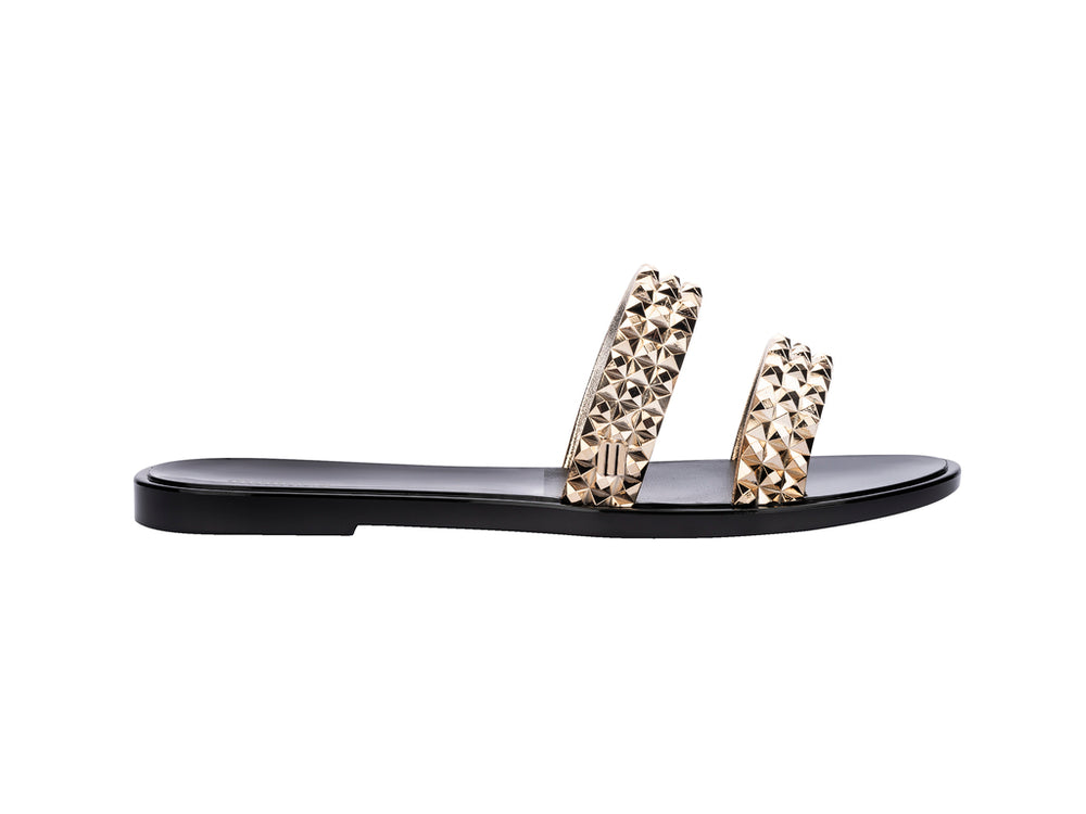 Sandalias negras Melissa con tiras adornadas con tachuelas doradas brillantes.