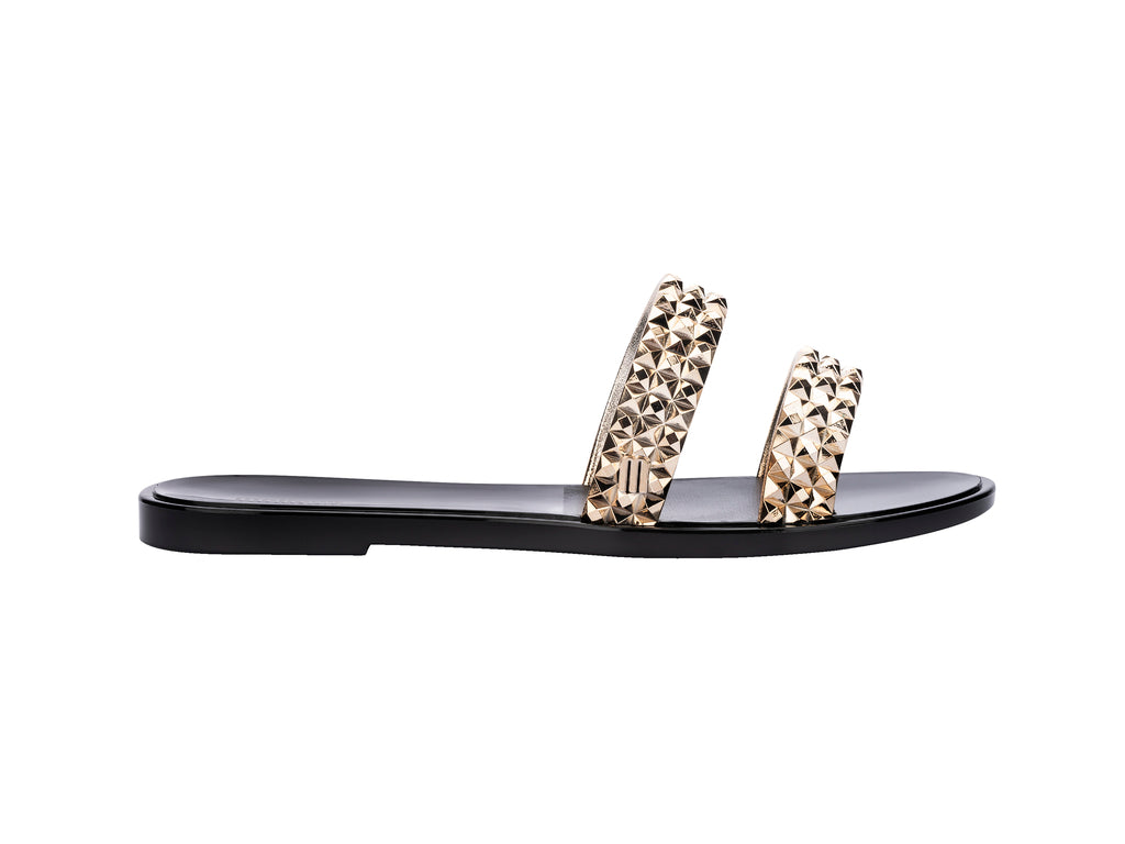 Sandalias negras Melissa con tiras adornadas con tachuelas doradas brillantes.