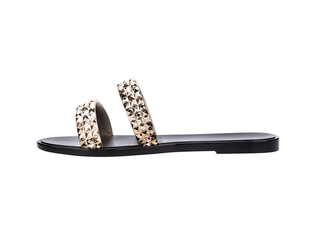 Sandalias negras Melissa con tiras adornadas con tachuelas doradas brillantes.
