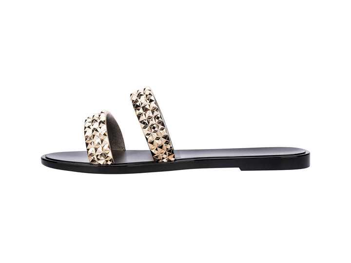 Sandalias negras Melissa con tiras adornadas con tachuelas doradas brillantes.
