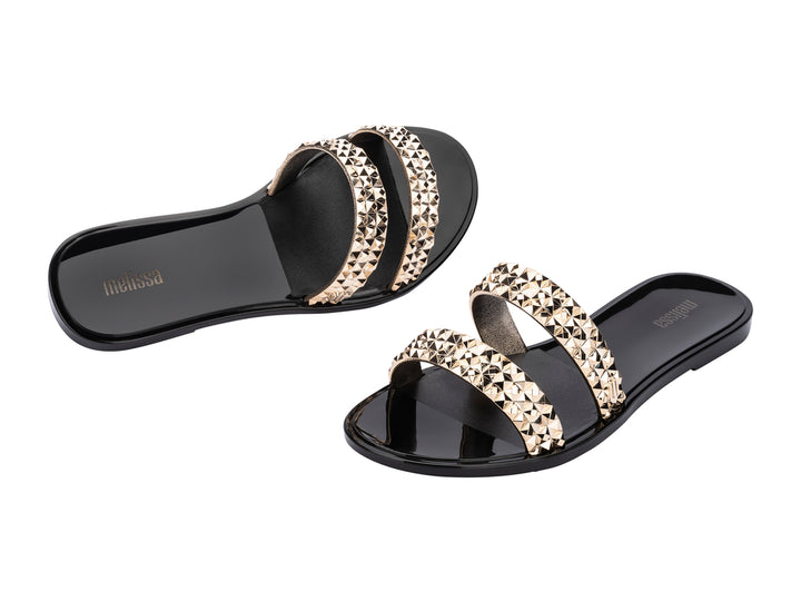Sandalias negras Melissa con tiras adornadas con tachuelas doradas brillantes.