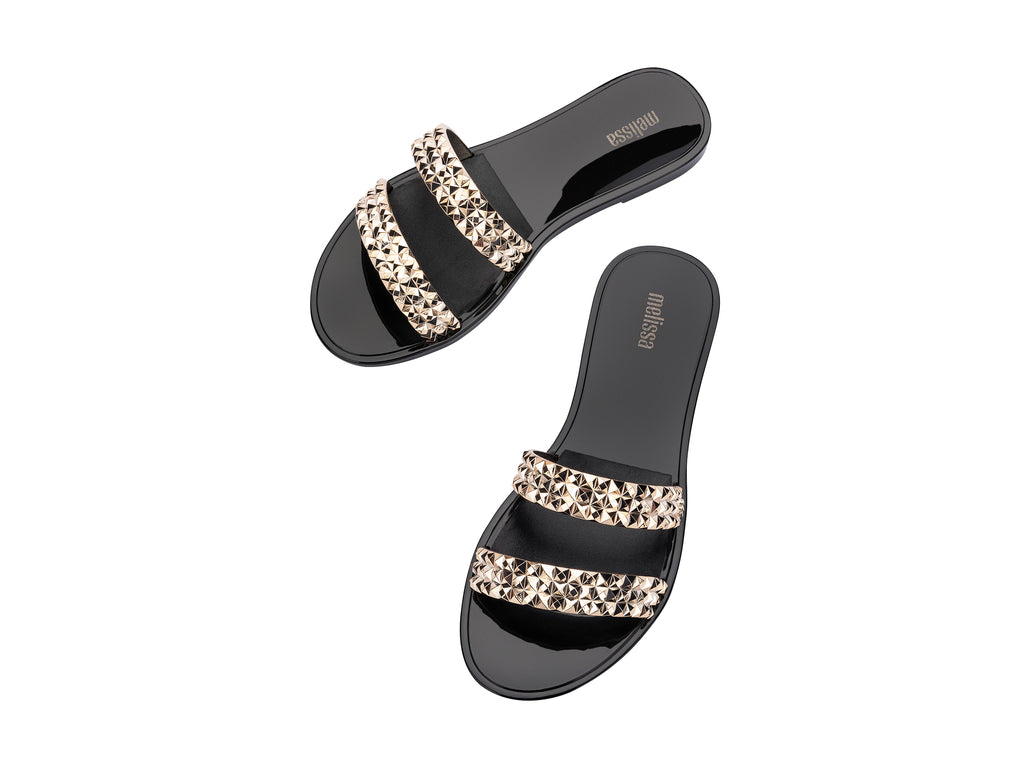 Sandalias negras Melissa con tiras adornadas con tachuelas doradas brillantes.
