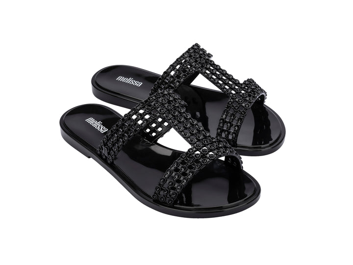 Sandalias Melissa Glowing Slide en color negro brillante con tiras decorativas entrelazadas.