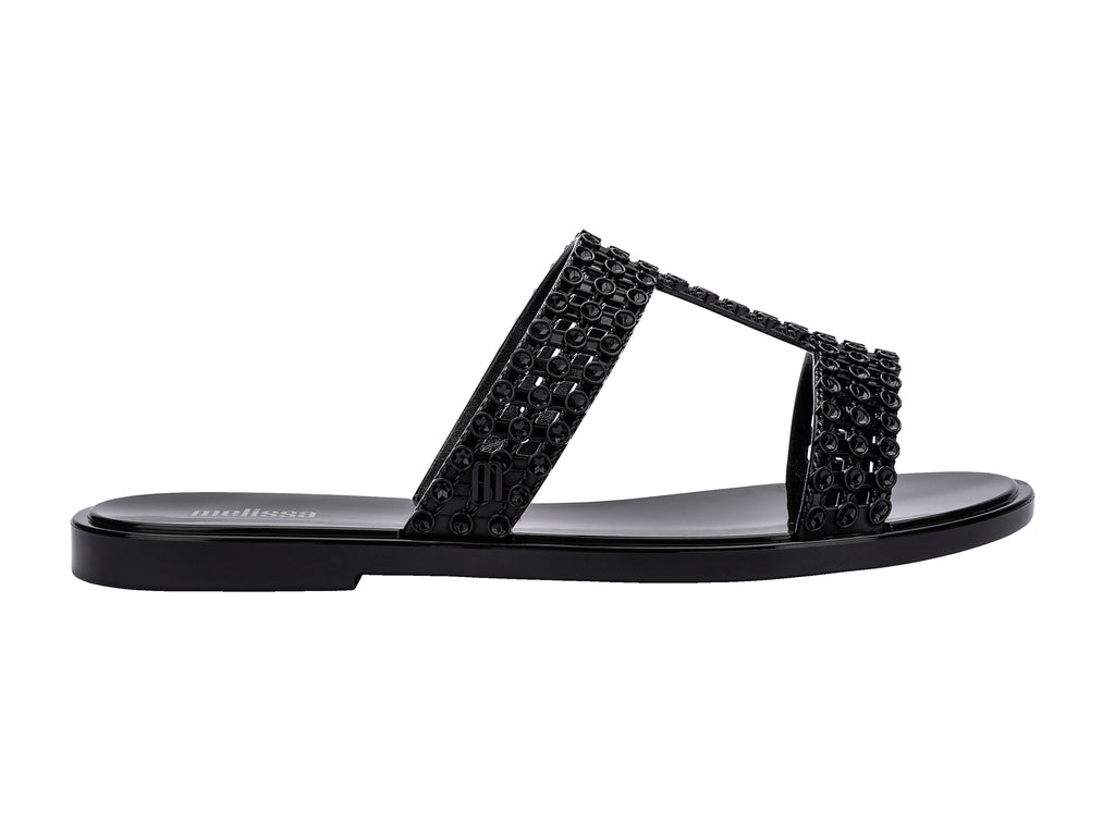 Sandalias Melissa Glowing Slide en color negro brillante con tiras decorativas entrelazadas.