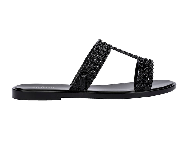 Sandalias Melissa Glowing Slide en color negro brillante con tiras decorativas entrelazadas.