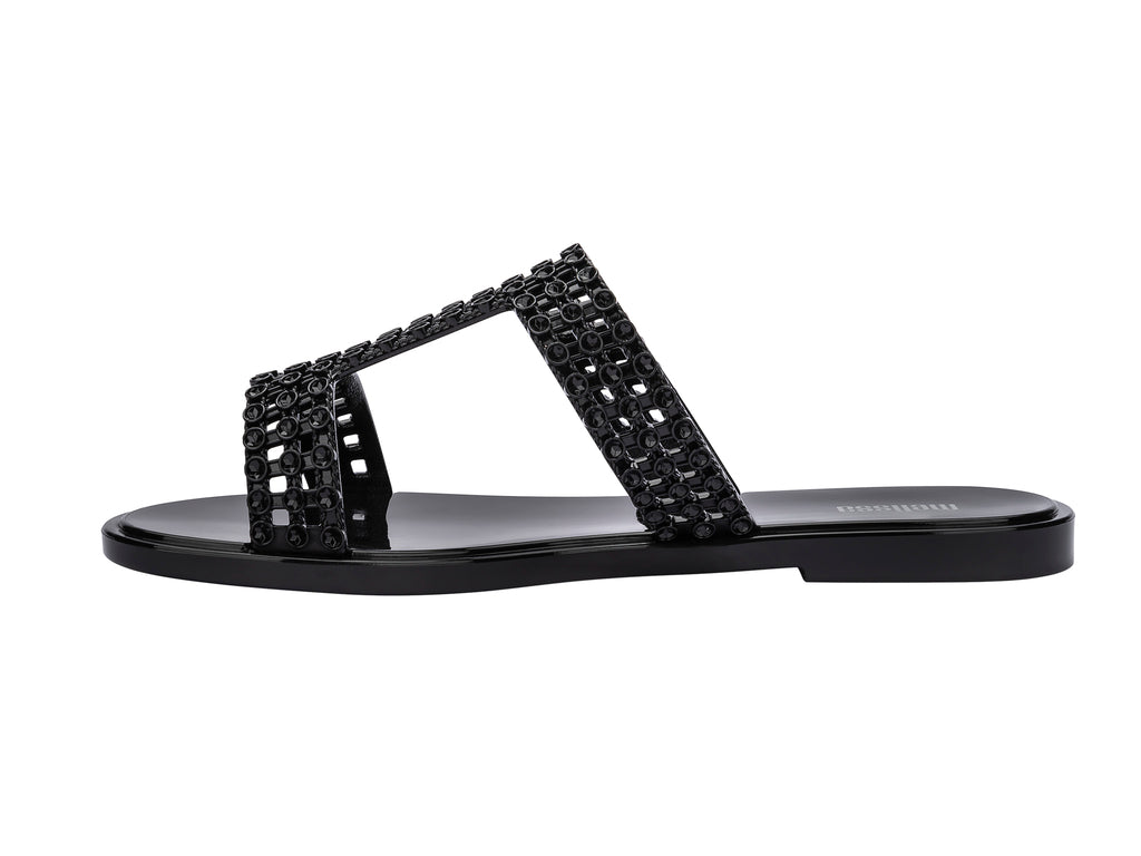Sandalias Melissa Glowing Slide en color negro brillante con tiras decorativas entrelazadas.