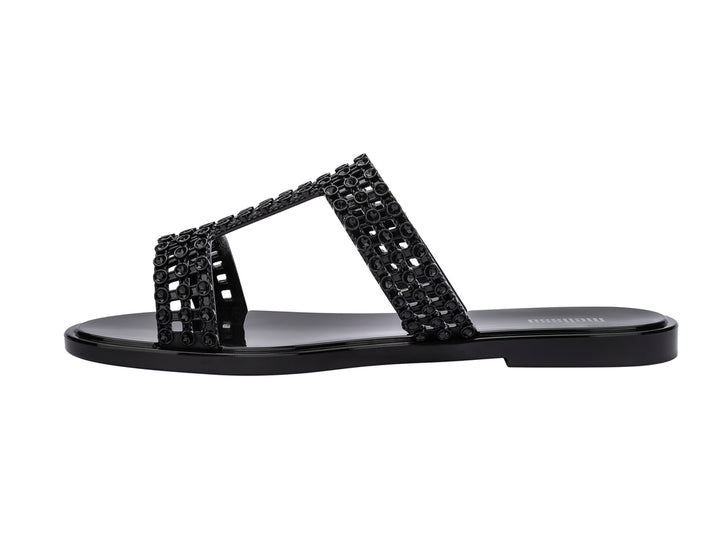 Sandalias Melissa Glowing Slide en color negro brillante con tiras decorativas entrelazadas.