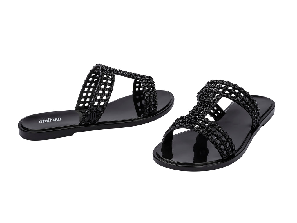 Sandalias Melissa Glowing Slide en color negro brillante con tiras decorativas entrelazadas.