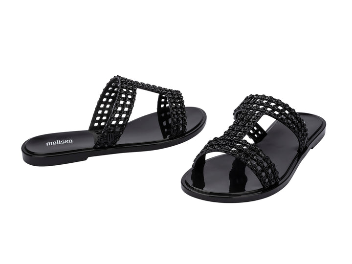 Sandalias Melissa Glowing Slide en color negro brillante con tiras decorativas entrelazadas.