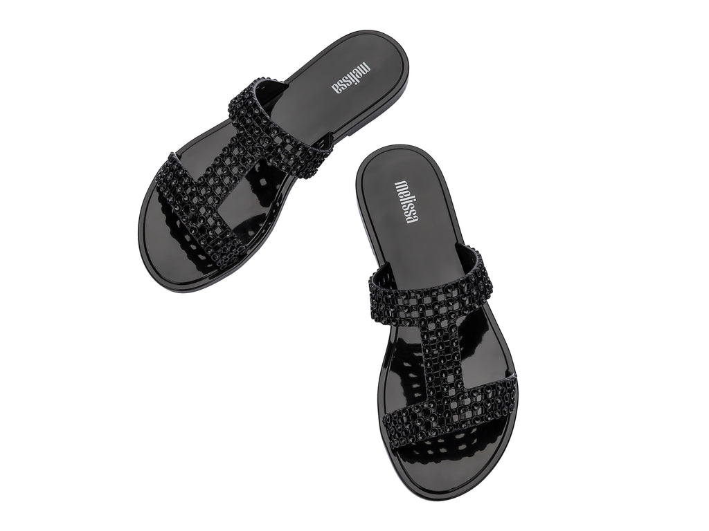 Sandalias Melissa Glowing Slide en color negro brillante con tiras decorativas entrelazadas.