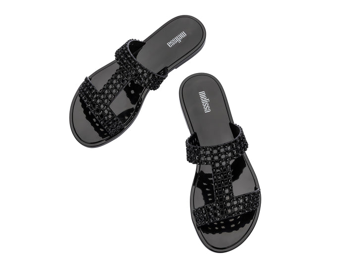 Sandalias Melissa Glowing Slide en color negro brillante con tiras decorativas entrelazadas.