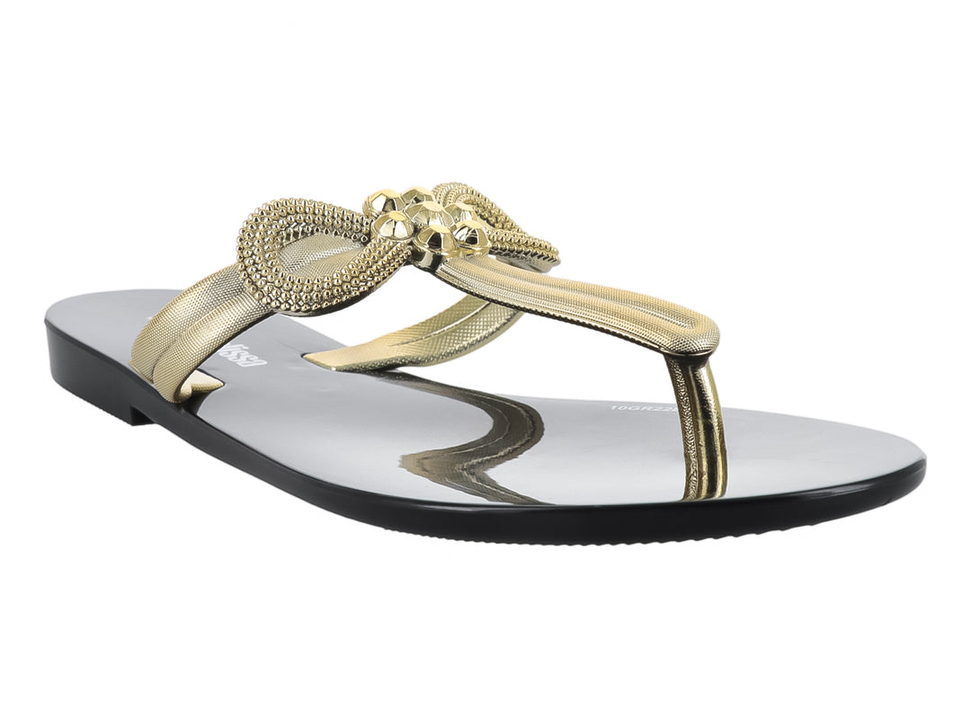 Sandalia infantil Mini Melissa de suela negra brillante y tiras doradas con un moño decorativo.