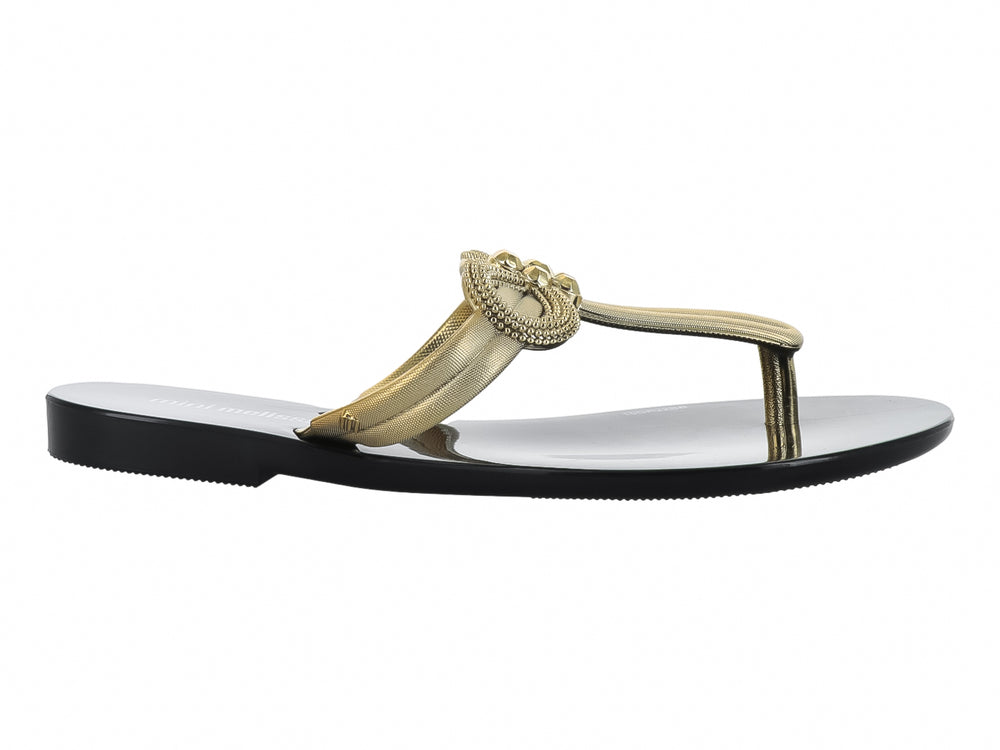 Sandalia infantil Mini Melissa de suela negra brillante y tiras doradas con un moño decorativo.