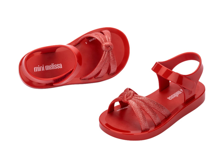 Sandalia infantil Mini Melissa de color rojo con tiras frontales brillantes y correa ajustable.