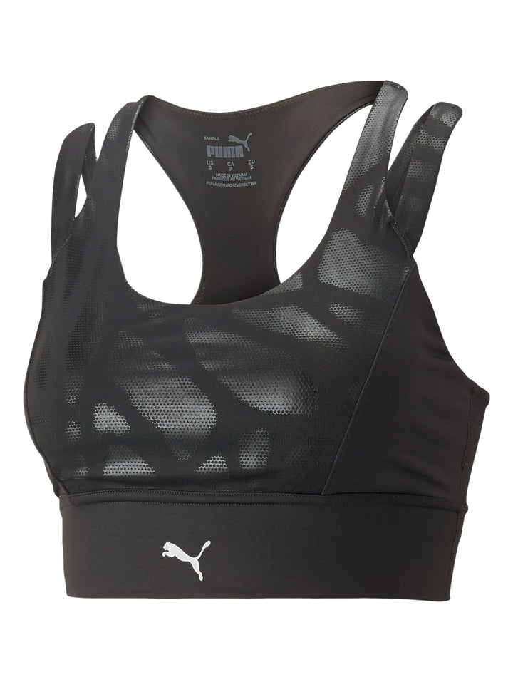 Mujer vistiendo un top deportivo PUMA color negro brillante de impacto medio con tirantes y logo frontal.