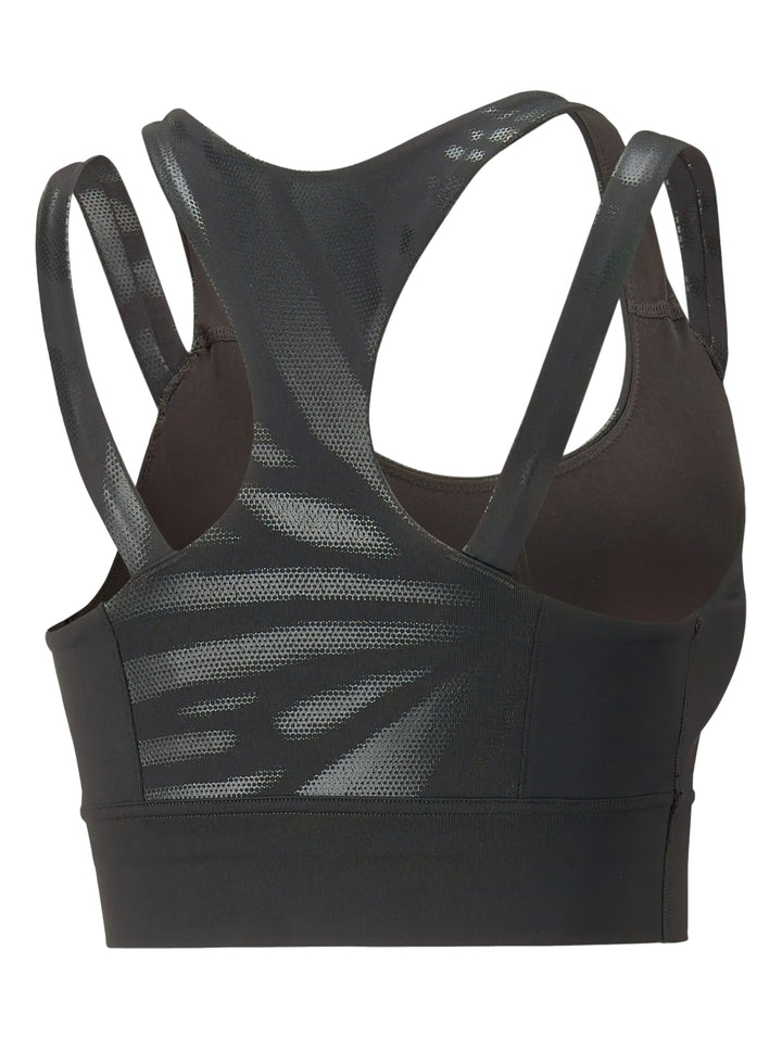 Mujer vistiendo un top deportivo PUMA color negro brillante de impacto medio con tirantes y logo frontal.