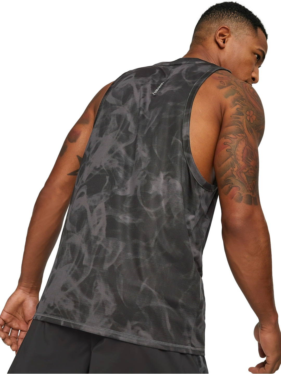 Hombre usando camiseta sin mangas PUMA negra con estampado abstracto y shorts deportivos.