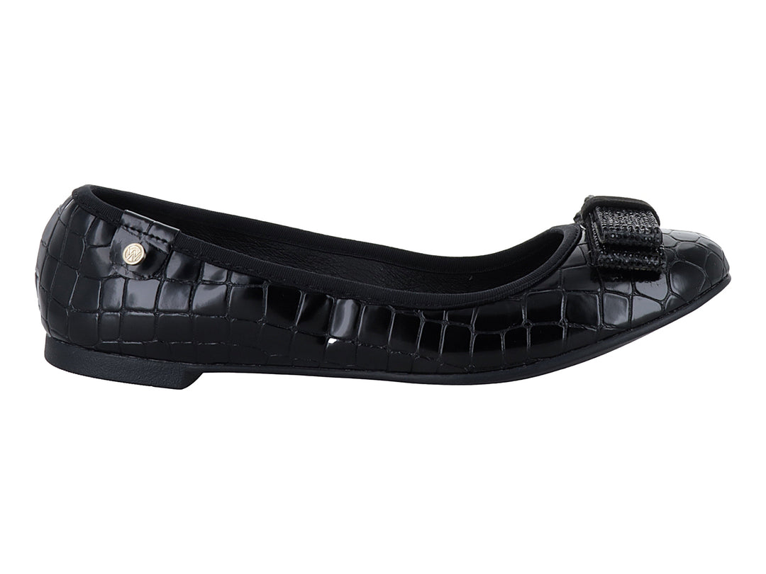 Zapato plano negro con textura de cocodrilo y moño decorativo frontal.