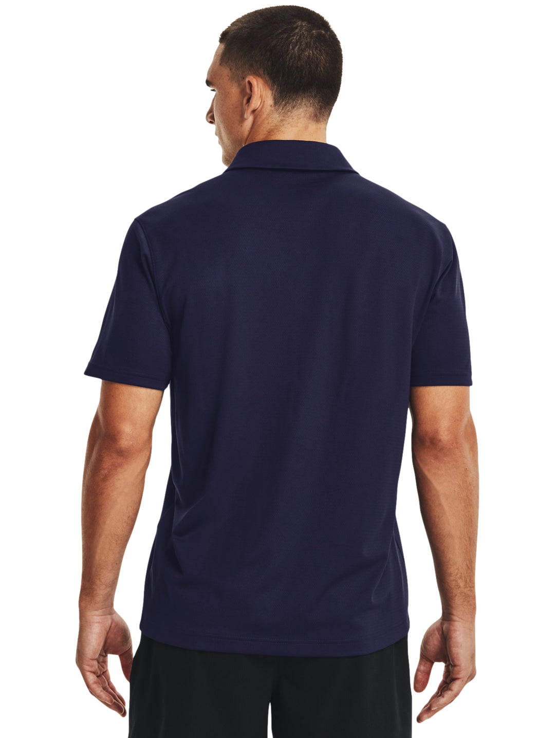 Hombre vistiendo polo deportivo Under Armour de color azul marino con logotipo blanco en el pecho.